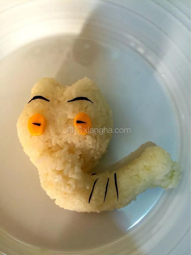 利用保鲜膜制作一个圆形白色饭团，用筷子在饭团顶端向下压形成大象头顶，用芝士片和海苔剪出眼睛
继续制作一个长条饭团，一端用筷子向里压形成大象的长鼻子，轻轻将饭团折弯和头链接好，用芝士片剪出耳朵
