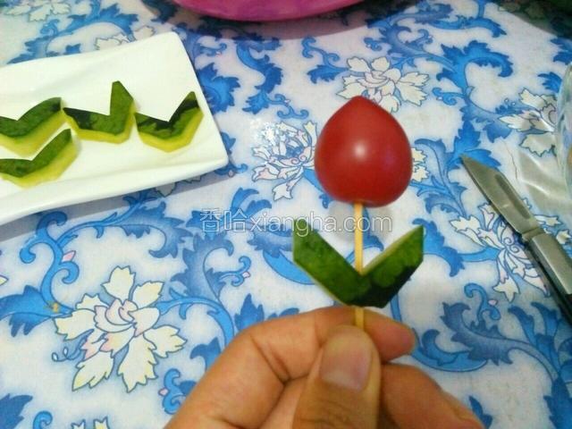 用牙签将西瓜皮做的叶子和圣女果穿连起来，这样就成了一朵花