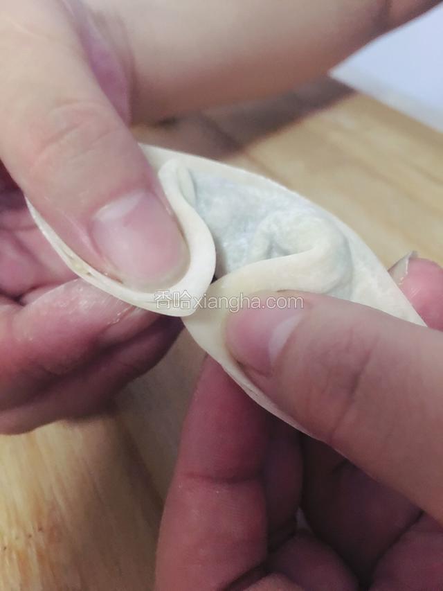 用手捏着前面两个角，小拇指挑着后面的饺子皮，把前面两个角捏在一起