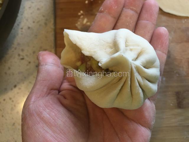 左手托着装满馅的包子皮，右手拇指和食指分别捏住包子皮边缘的上下面，转圈捏紧包子皮，两手搭配分别向相反的方向转，如图。