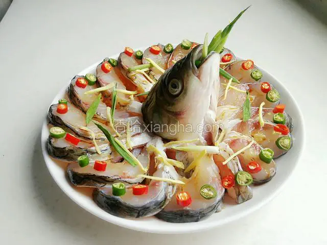 然后把蒸鱼豉油倒入碗里，用勺子浇豉油，尽量将每一片鱼都浇上，包括鱼头。青红美人椒摆放在每片鱼肉上，接着取一半的姜丝和葱段撒在鱼上面，再塞点在鱼嘴里。