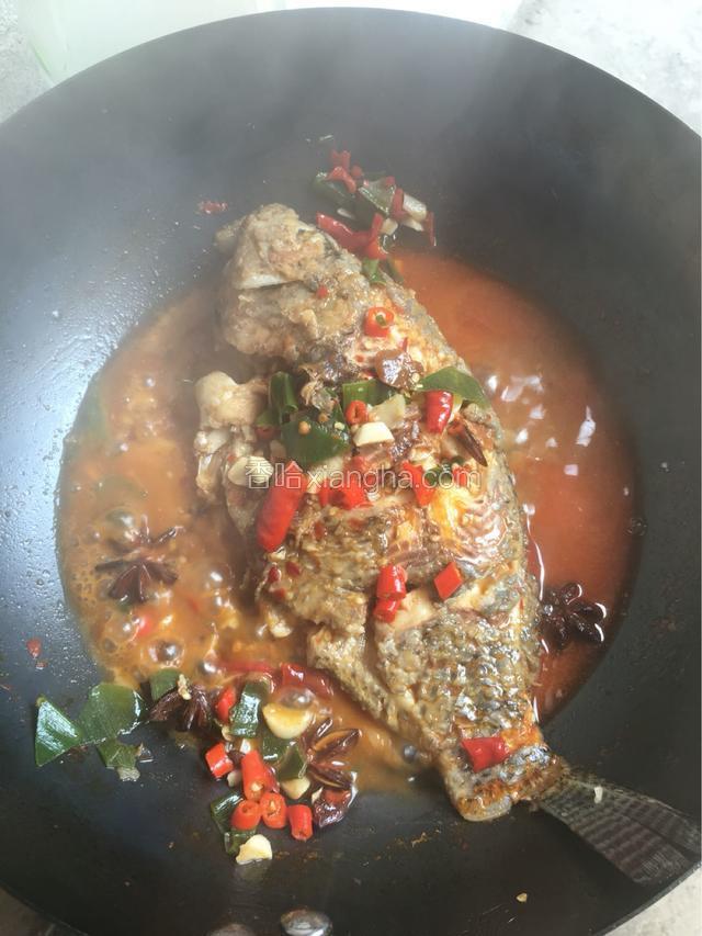 轻晃炒锅，避免鱼粘锅底，把鱼翻身，换另一面浸入汤汁，中火收汁