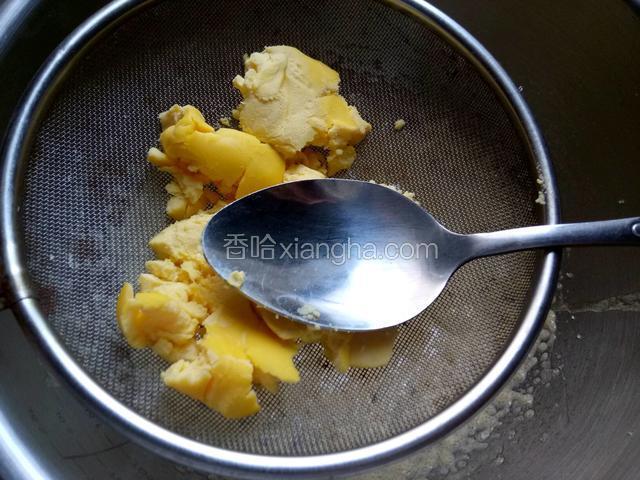 将2个蛋黄用勺子在筛子上压碾。