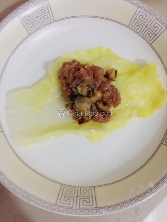 白菜叶摊开，放入适量的肉馅，从根部往上卷。
