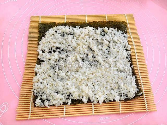 用饭勺将米饭均匀平铺在紫菜上但不要太厚，最后留一节手指长的紫菜不要铺米饭，留着封口用。