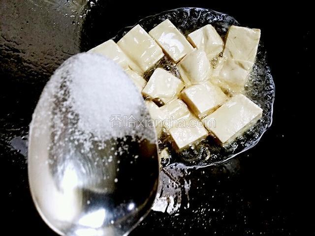接着，改小火，然后用汤匙挖一克盐，用手均匀撒在豆腐上煎制，这样是让豆腐起入味的作用