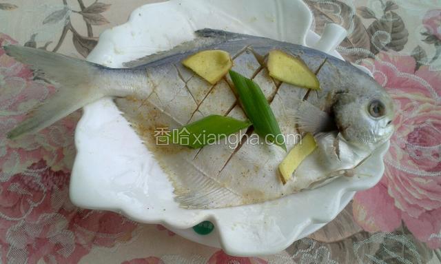 在鱼两侧打上十字花刀，洒上点盐，胡椒粉抹匀，再放上葱姜腌制十分钟