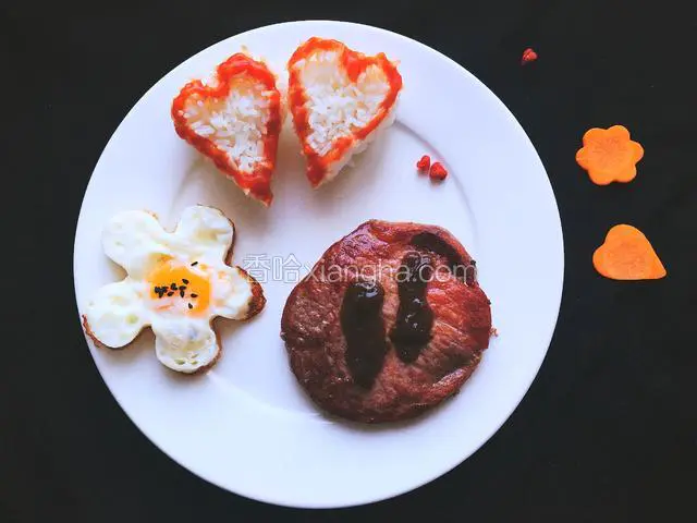 摆盘一，花型鸡蛋上撒少许黑芝麻，牛排上涂上黑椒酱汁，心形米饭摆好即可。中间两个红色的小心型是用枸杞捏制的。
