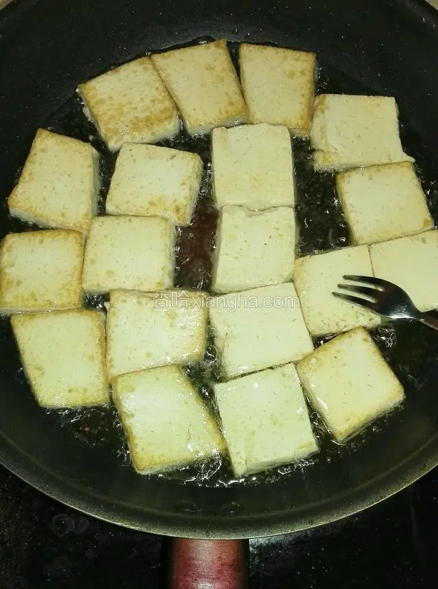 切好的豆腐入油锅稍微煎治一下，用餐叉在每块豆腐上扎上小孔。煎的时间火不要大，时间也不要长，微黄即可，盛出备用