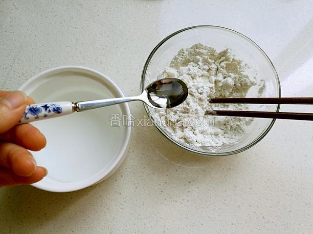 面粉放在碗里，一边用筷子搅拌，一边用勺子一点点加水。
