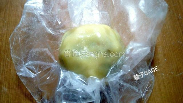 提起保鲜膜的四周，将饼皮包裹好五仁馅。并用手均匀的推开饼皮，边推边把饼皮厚的部分推均匀，直到把馅料全部包裹住。 