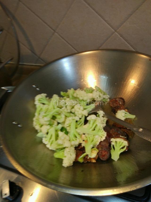 把香肠放入翻炒片刻后。把花菜和青辣椒也放入一起翻炒三分钟左右！
