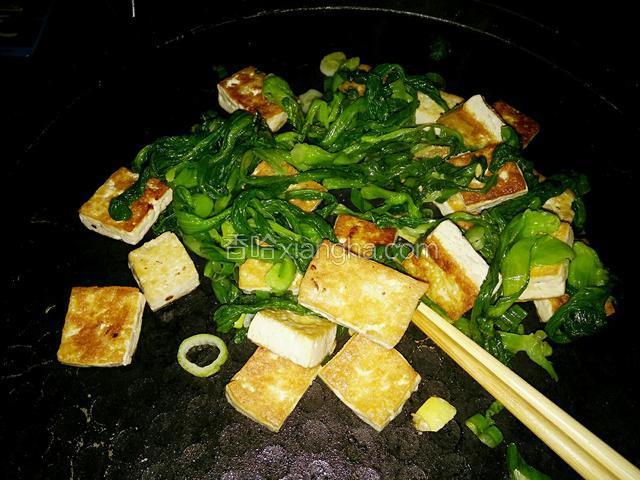 接着把煎好的豆腐与油菜一块翻炒，放入盐和味精。再炒一分钟即可关火