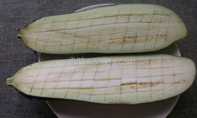茄子洗净从中间对半切开，用小刀在茄子里面如图划成小方块，茄子皮不要划破