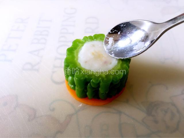 将胡萝卜片垫在苦瓜下面，用勺子挖出山药泥将苦瓜填满。