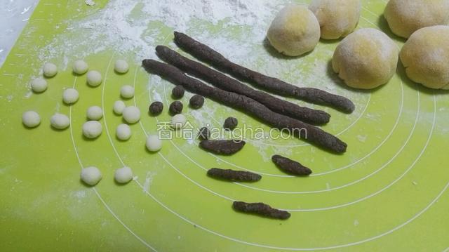 再把可可粉面团搓成长15CM的长条，还有3CM弯弯的月儿；白色面团和可可粉面团分别揪一团搓成多个小圆球，然后压瘪成眼睛。