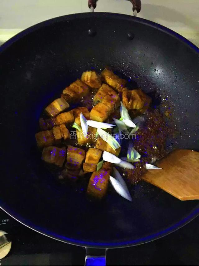 倒入五花肉快速翻炒，让每块五花肉都均匀的裹上糖色加入葱段，料酒，少许红烧酱油，八角，香叶，干树椒翻炒均匀。
