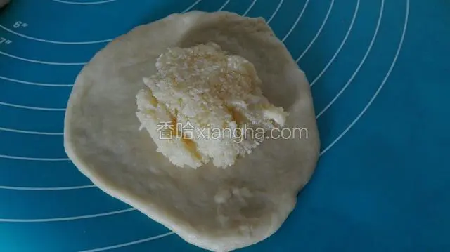  取出一个面团，擀成饼。把提前制作好的椰蓉馅放在中间。椰蓉馅制作方法为：椰蓉，玉米油，牛奶，白糖混合拌匀