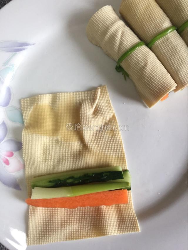开始卷豆腐皮。取一张豆腐皮，在短边处放黄瓜、胡萝卜、大葱丝，从下头卷起。