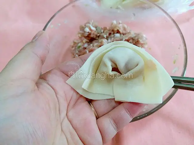 第三步再把对折后的皮两边向怀里一窝，将两角重叠在一起，按压便完成一个馄饨。