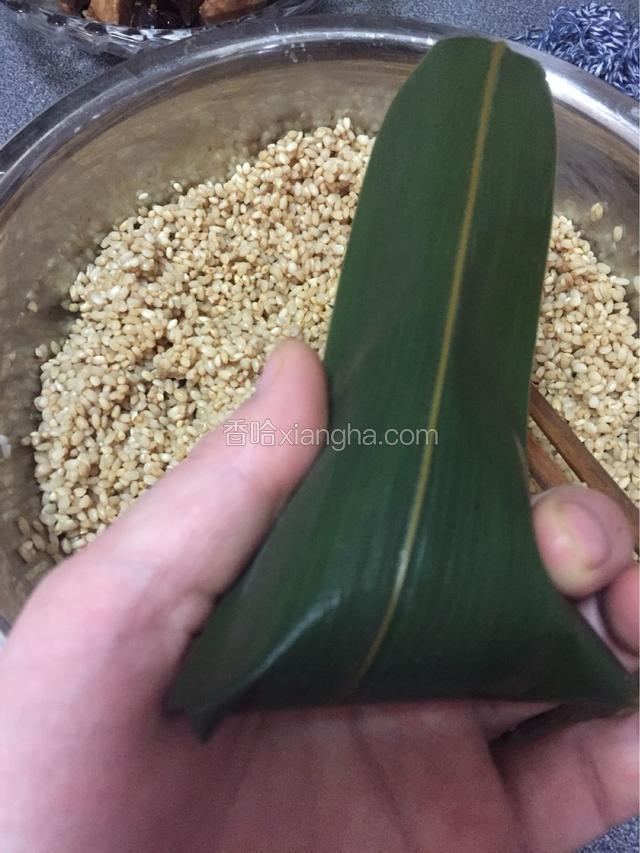左手夹住粽子的下方，右手把叶子轻轻地往下掖盖住糯米，不能太用力了，叶子太脆落容易开缝。
