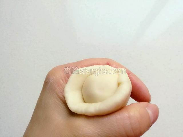 取一个油皮面团压扁，包入油酥，用虎囗慢慢往上收紧收口，然后搓圆。