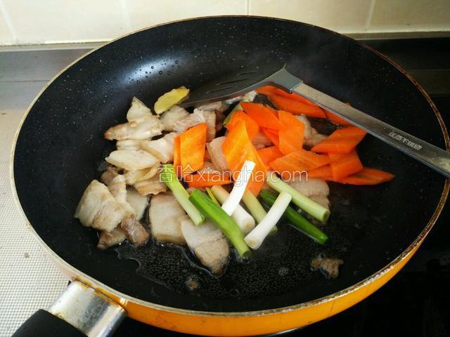 当五花肉出现微焦时，放入胡萝卜片和青蒜白。