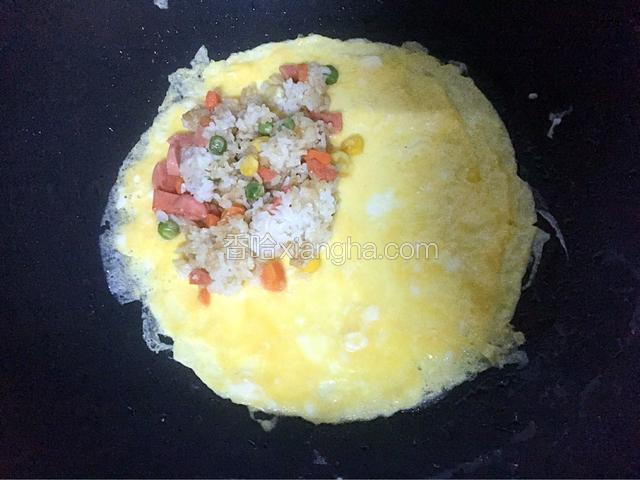 小火煎至表面蛋液凝固时，把炒饭放在鸡蛋的一边