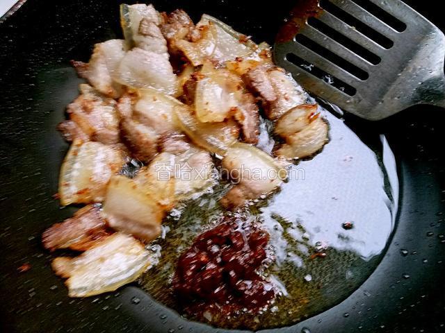 锅内五花肉煸炒出油，且变的焦黄时，调小火，把豆瓣酱下锅，用锅铲把豆瓣酱炒出红油。
