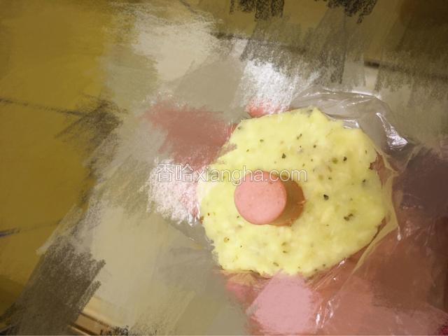 戴上一次性手套抓适量用手压成小圆饼，中间竖放一个烤肠，然后用手把四周土豆泥捏在烤肠上。