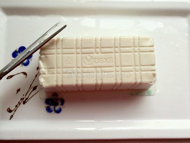 豆腐撕去塑料封盖，倒扣在盘中，用剪刀在盒子的四角剪去小孔。