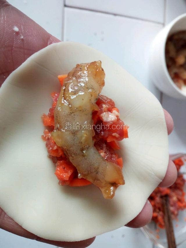 手上放一个饺子皮，先放上肉馅，再放上一个虾，用包饺子的方法包拢。