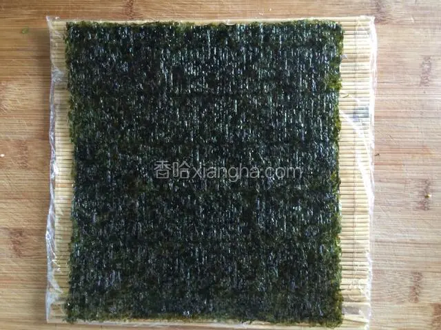 竹帘包上保鲜膜，取一张海苔铺在上面，粗糙面朝上