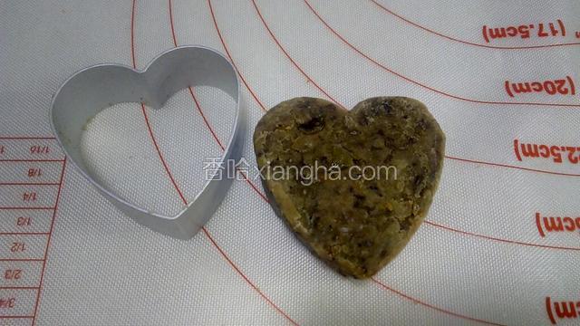 一手沿模具边缘轻轻往下按绿豆泥，另一手轻轻将模具向上提起，双手配合，一点点地把模具拿出来，一个心形的绿豆糕就做成了。