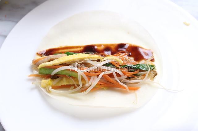 薄饼上抹上些许甜面酱。将炒好的合菜、鸡蛋丝码在饼皮上。