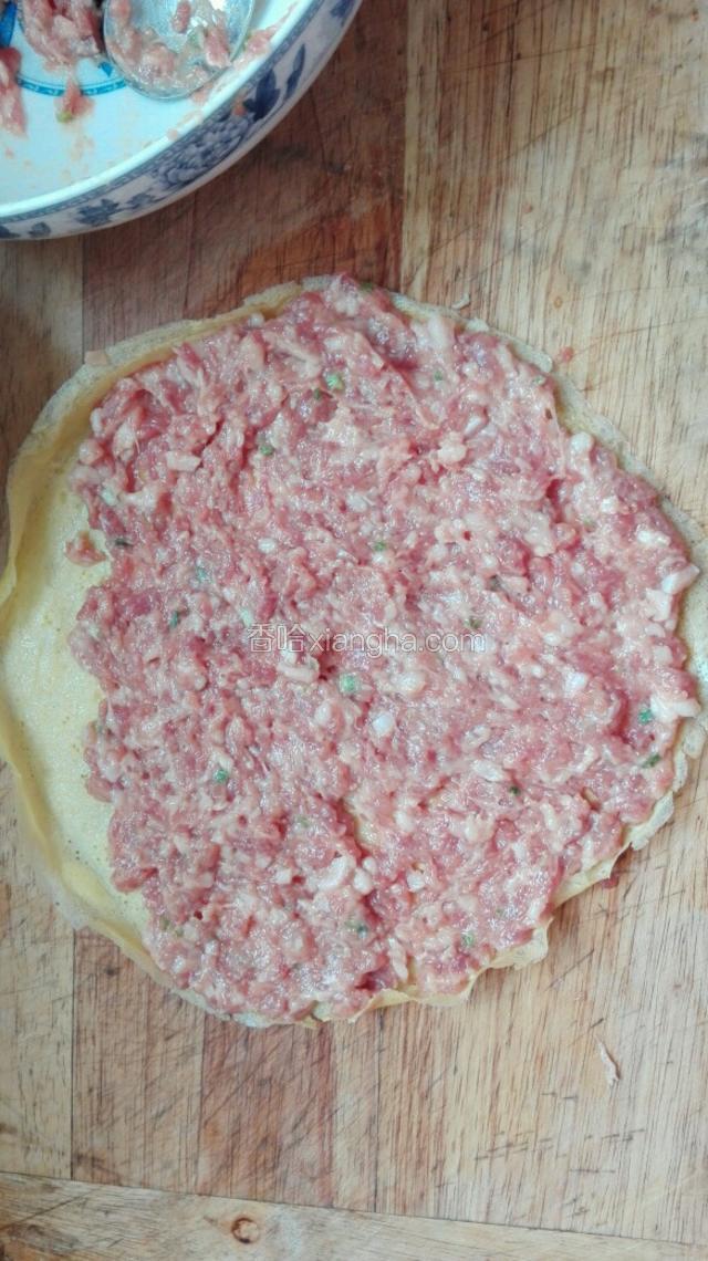 将肉馅用小勺一点一点均匀地平铺在鸡蛋薄饼上，末尾留一些空间不加肉馅。