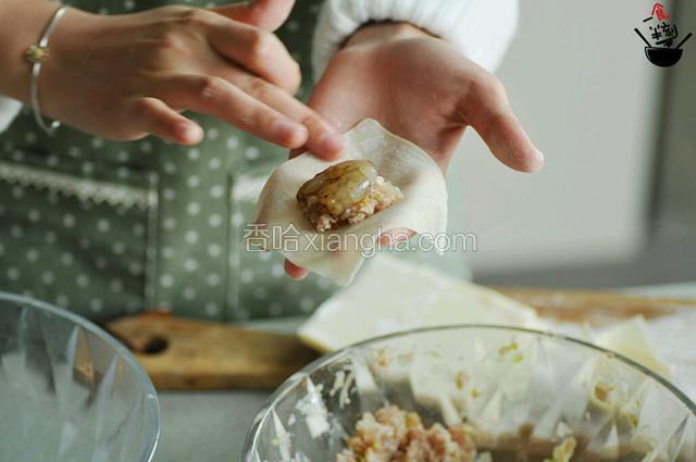 把云吞皮放在手心，放入少量肉糜，夹一只大虾，周围抹上少许清水