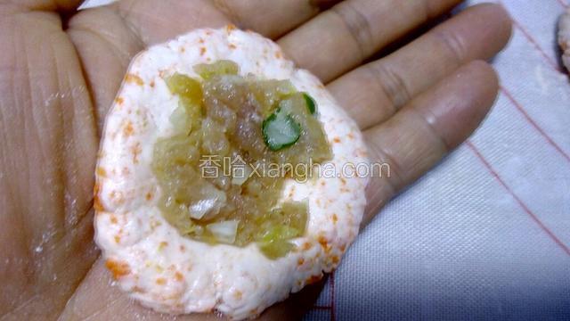 另一只手用勺子取适量肉馅，放于面皮中间凹窝处，然后把面皮从四周向上合拢，捏紧，把肉饺包在里边，包严实，不能露馅。