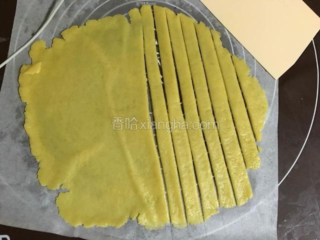 趁派底晾凉时来做派面，取出预留的派面皮用手压扁后擀成圆形，并用刮刀利成0.8CM的长条状；