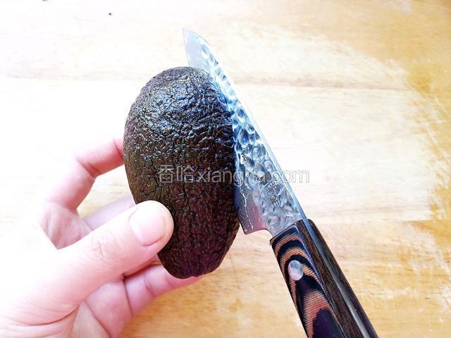 用手固定住牛油果的一边，用刀纵向围绕着核切割牛油果。