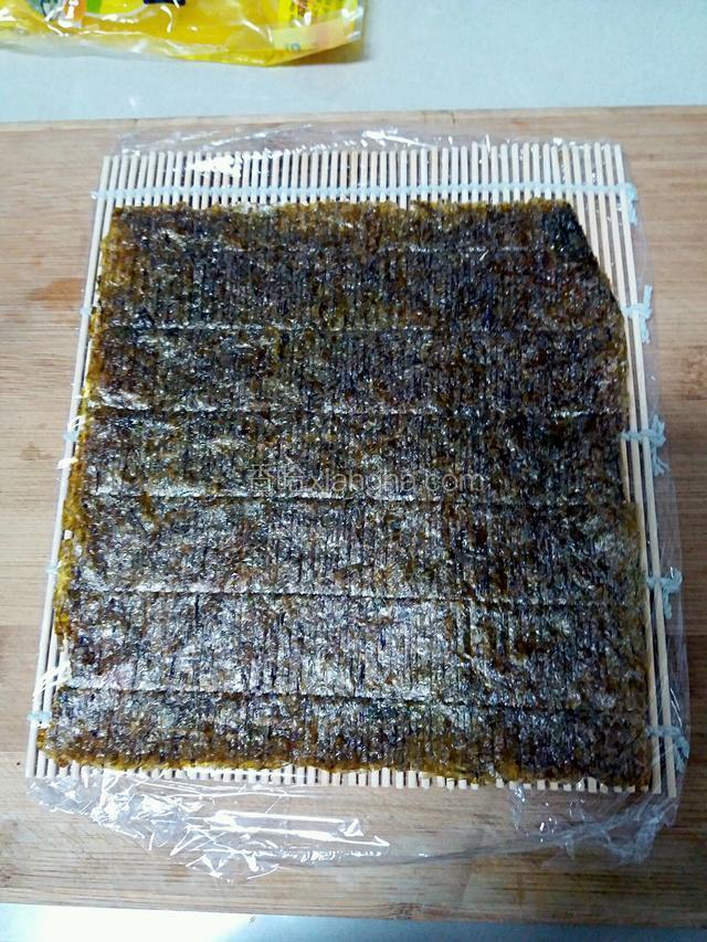 接着取一个寿司卷帘，用保鲜膜包起来（防止黏连），再铺上一张海苔，海苔粗糙面朝上。