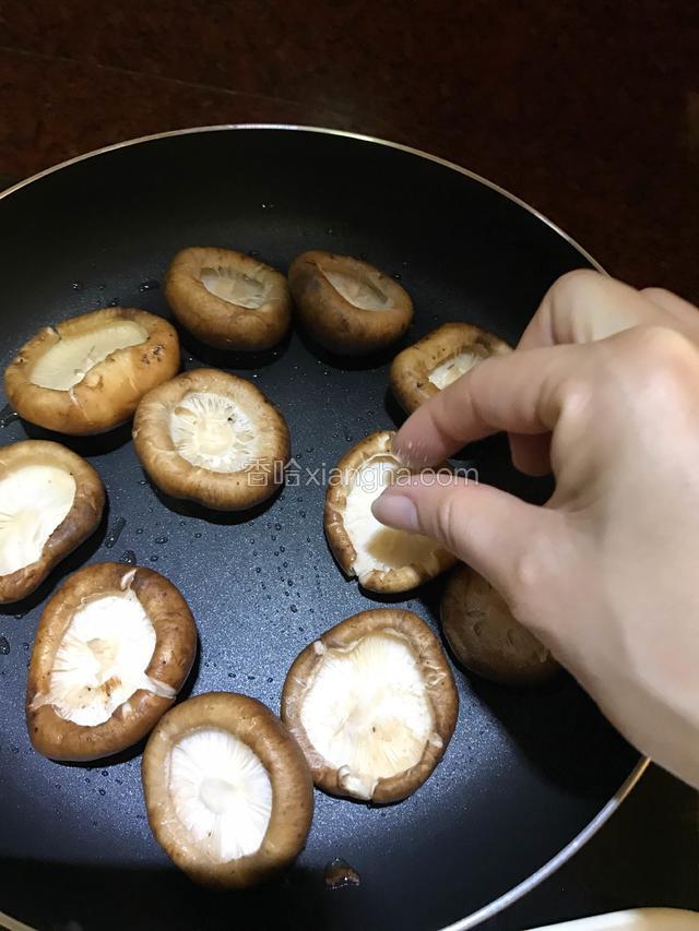 去蒂后的蘑菇整齐摆放在煎锅中，每一个蘑菇上放少许盐。