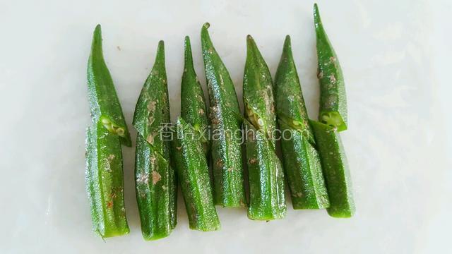 秋葵三分熟时即可盛出，放到切板上，每个秋葵一分为二。