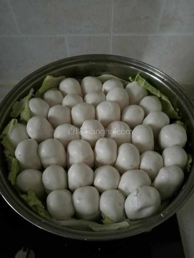 锅里铺上菜叶，涂上少许油，将做好的小圆球，轻轻揉成长椭圆形，一个个紧挨着放在锅里