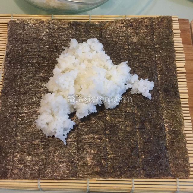 将寿司帘铺在台面上，放上一层寿司海苔，注意铺放海苔的走向，海苔上是有切纹的，要能顺着切纹切成段的走向才正确。上面铺一层薄薄的大米饭。