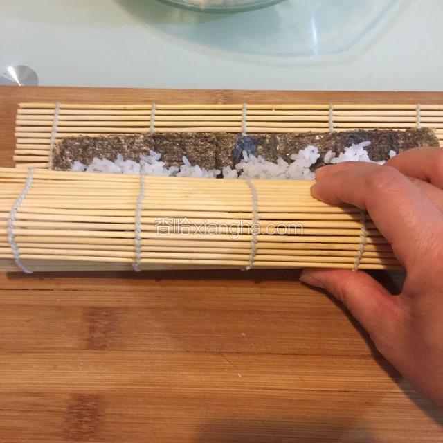 将海苔卷裹紧黄瓜条和肠条卷起来，利用竹帘向前推进。