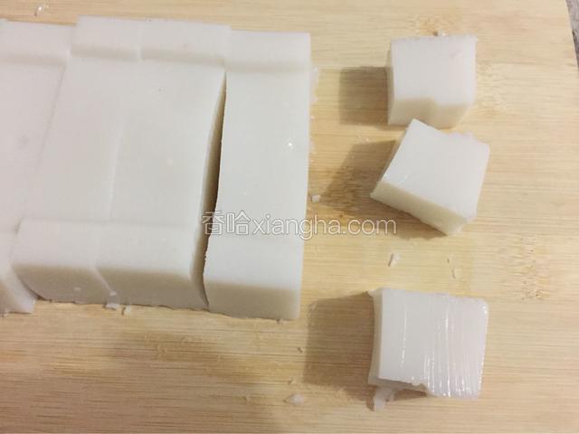 取出保鲜盒，用刀在四周划一划，再倒扣在砧板上，将椰汁块切成小方块。