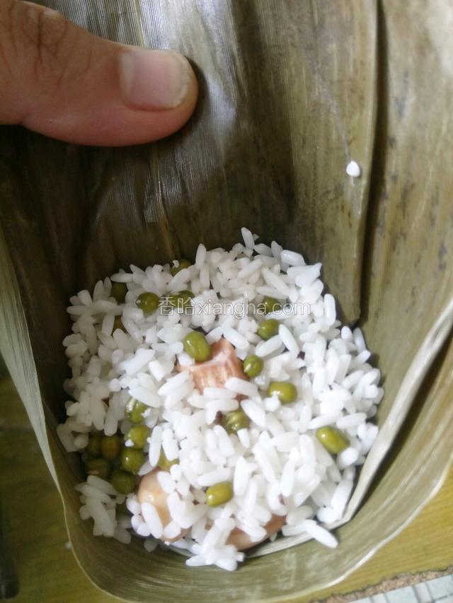 把两片粽叶折成漏斗状，放一半拌好的米装好。