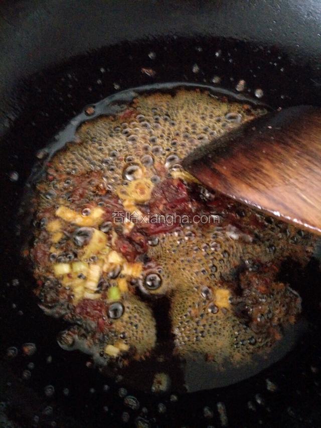 锅里的油放郫县豆瓣酱小火炒出红油，接着加入蒜片和葱花煸炒。