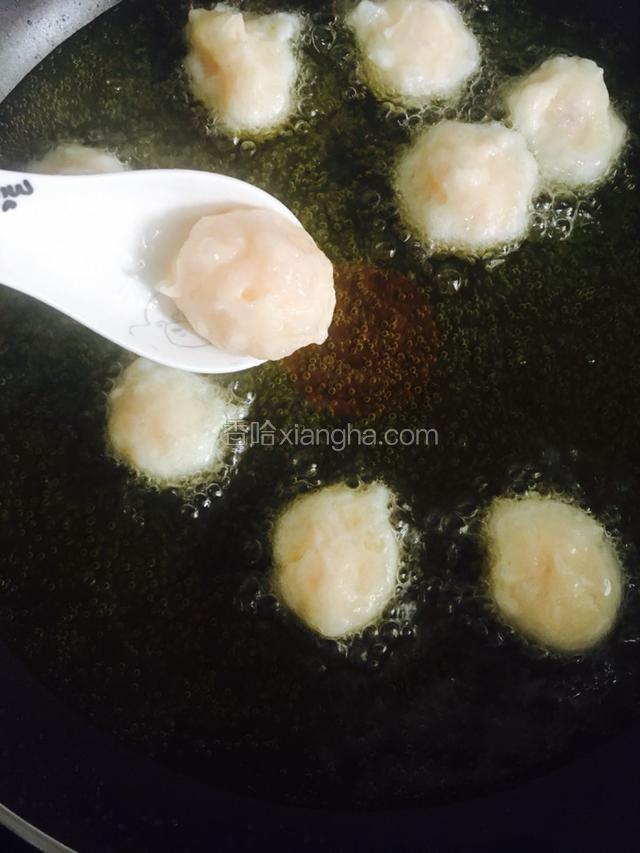 另外一个手拿小勺子把挤出来鱼丸舀入锅里。